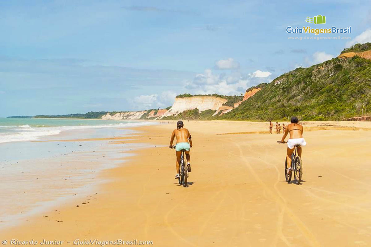 Imagem de duas pessoas andando de bicicleta na praia.