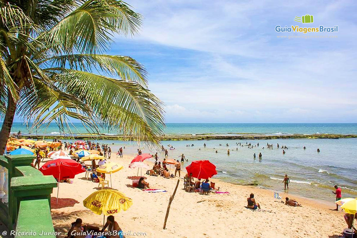 Imagem de visitantes no mar e nas areias da Praia de Arembepe.