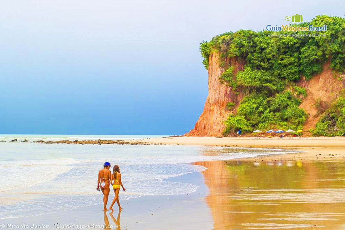 Imagem de mãe e filha caminhando na beira da Praia do Curral.