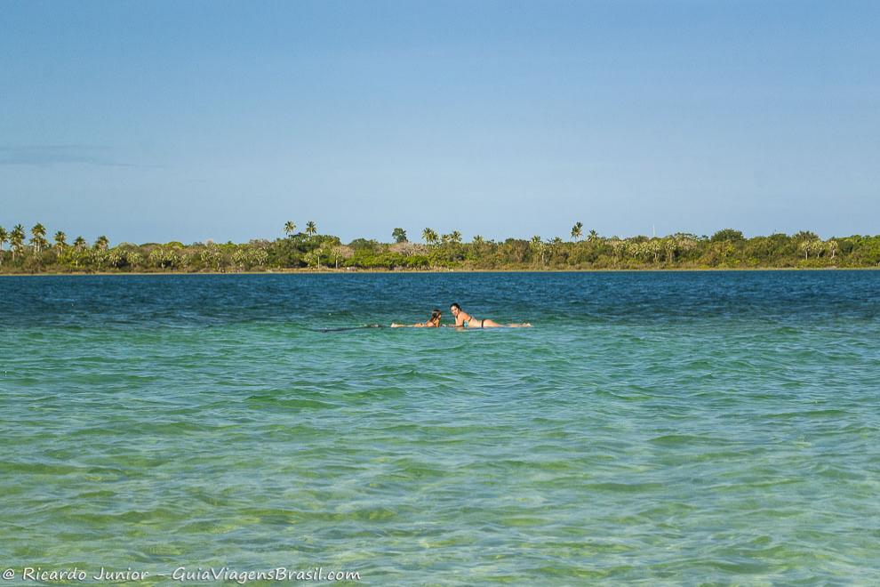 Imagem de mãe e filha deitadas no raso da lagoa, água cristalinas e azulzinha.