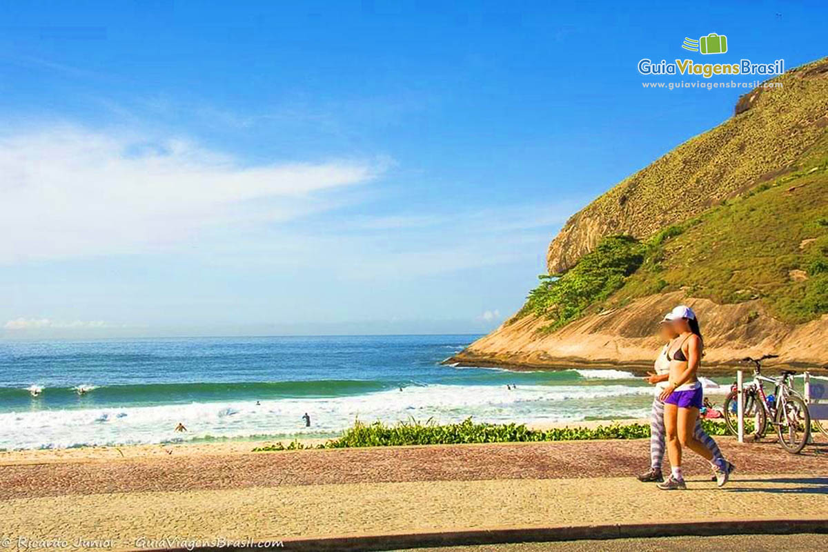 Imagem de amigas caminhando na Praia do Recreio dos Bandeirantes.