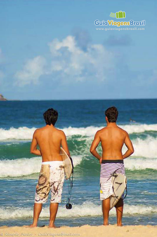 Imagem de amigos surfistas olhando para as ondas da praia.
