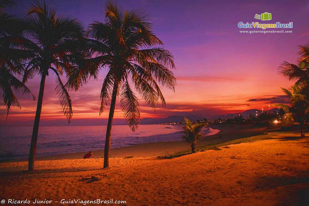 Imagem de um lindo anoitecer com céu alaranjado e lilás, na Praia da Vila em Saquarema.