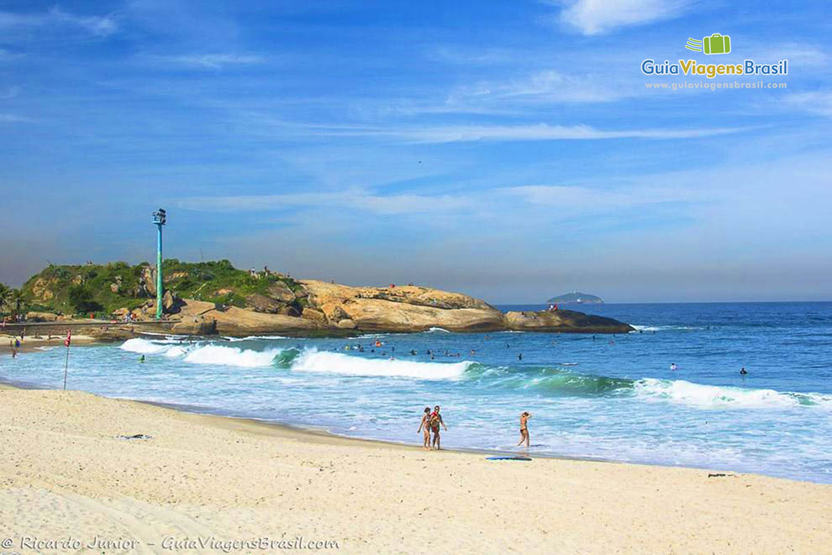 Imagem de pessoas andando nas areias claras da Praia Arpoador.