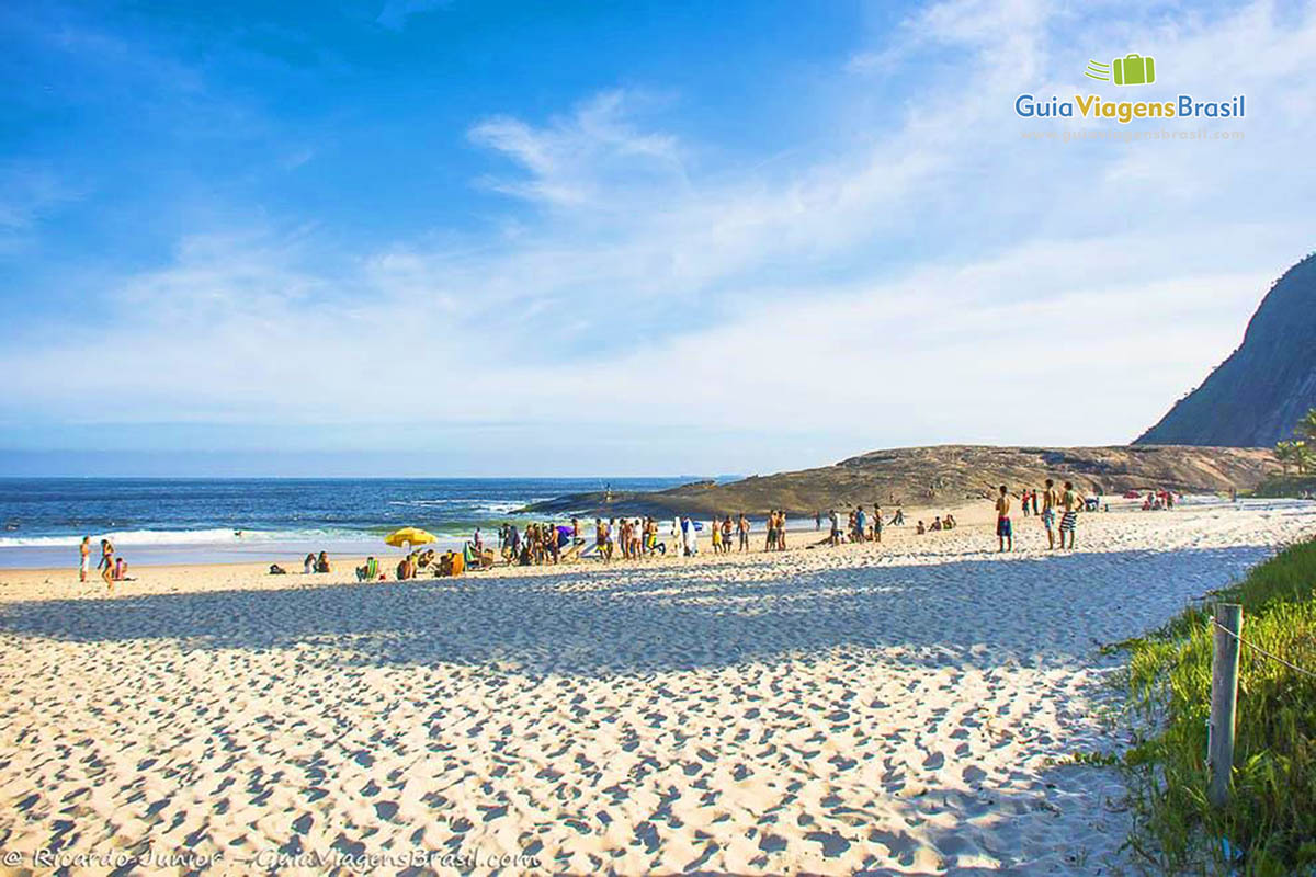 Imagem do canto da praia, mas possui faixa larga de areia e grande pedra.