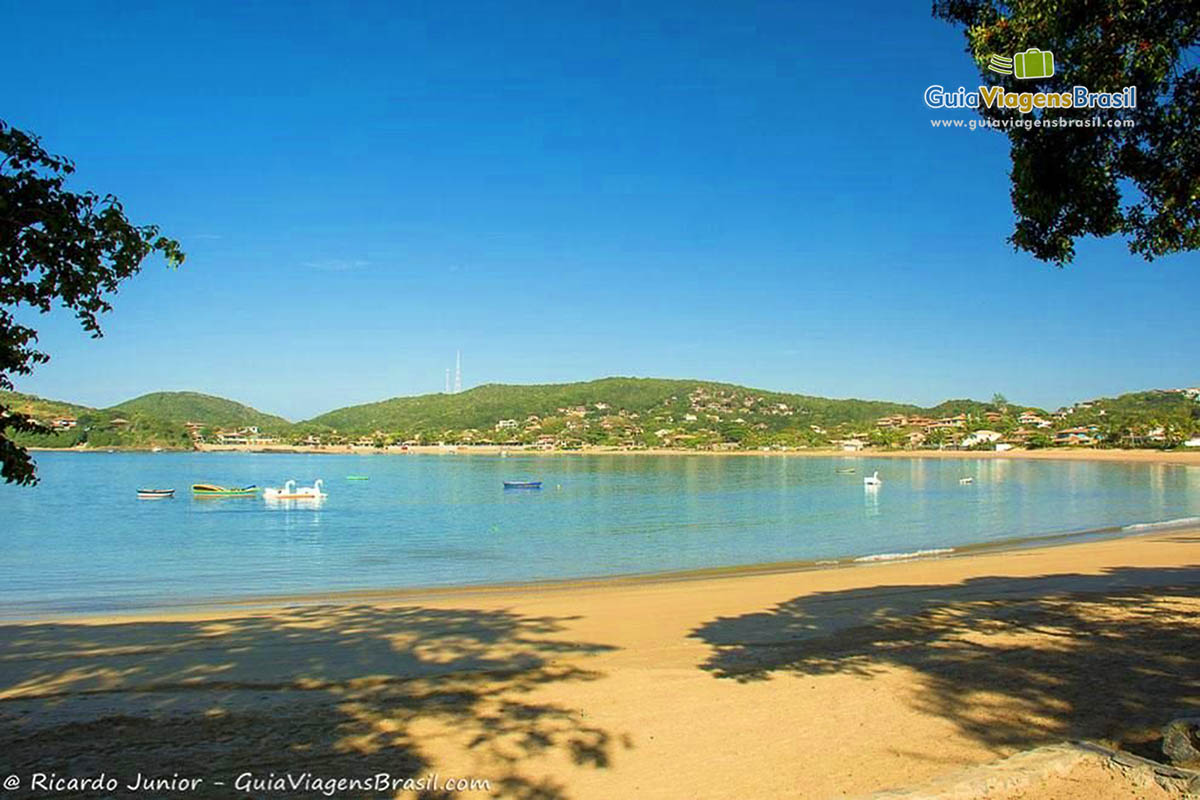 Imagem das sombra das árvores na areia da praia e o mar calmo ao fundo.