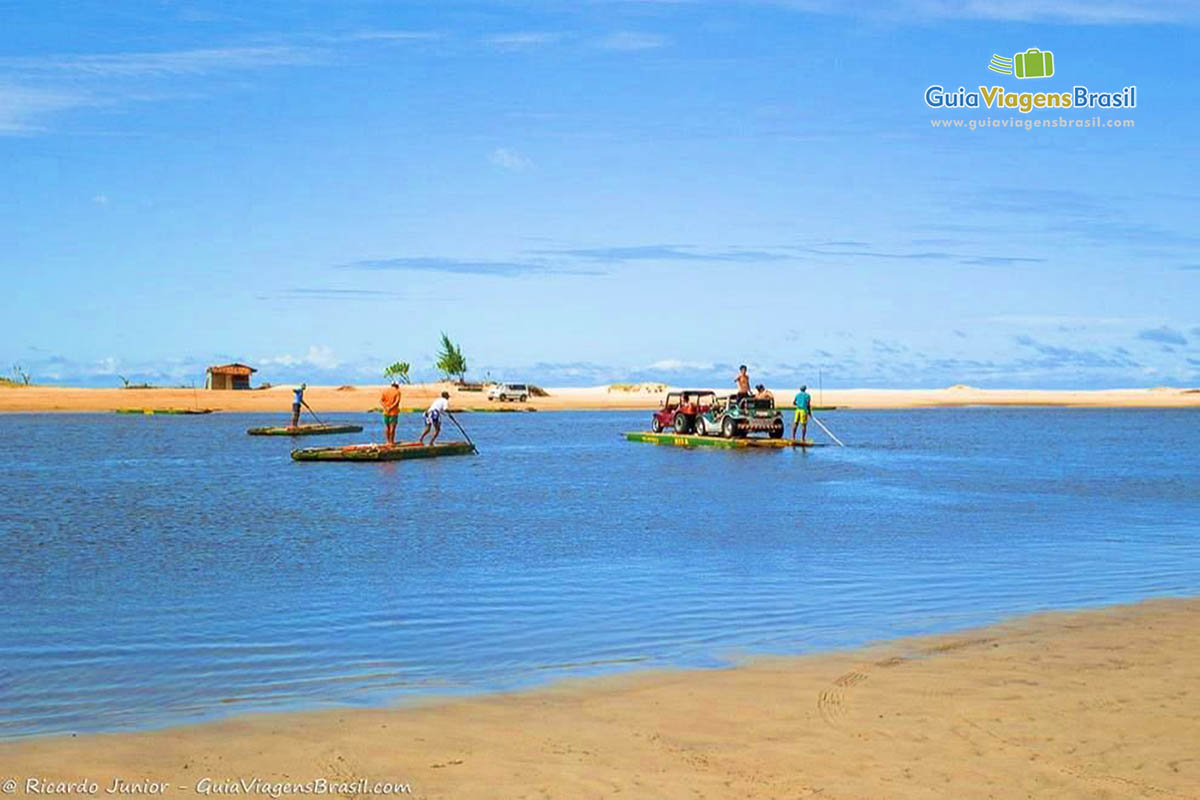 Imagem de dois carros em uma balsa e pescadores em seus barcos.