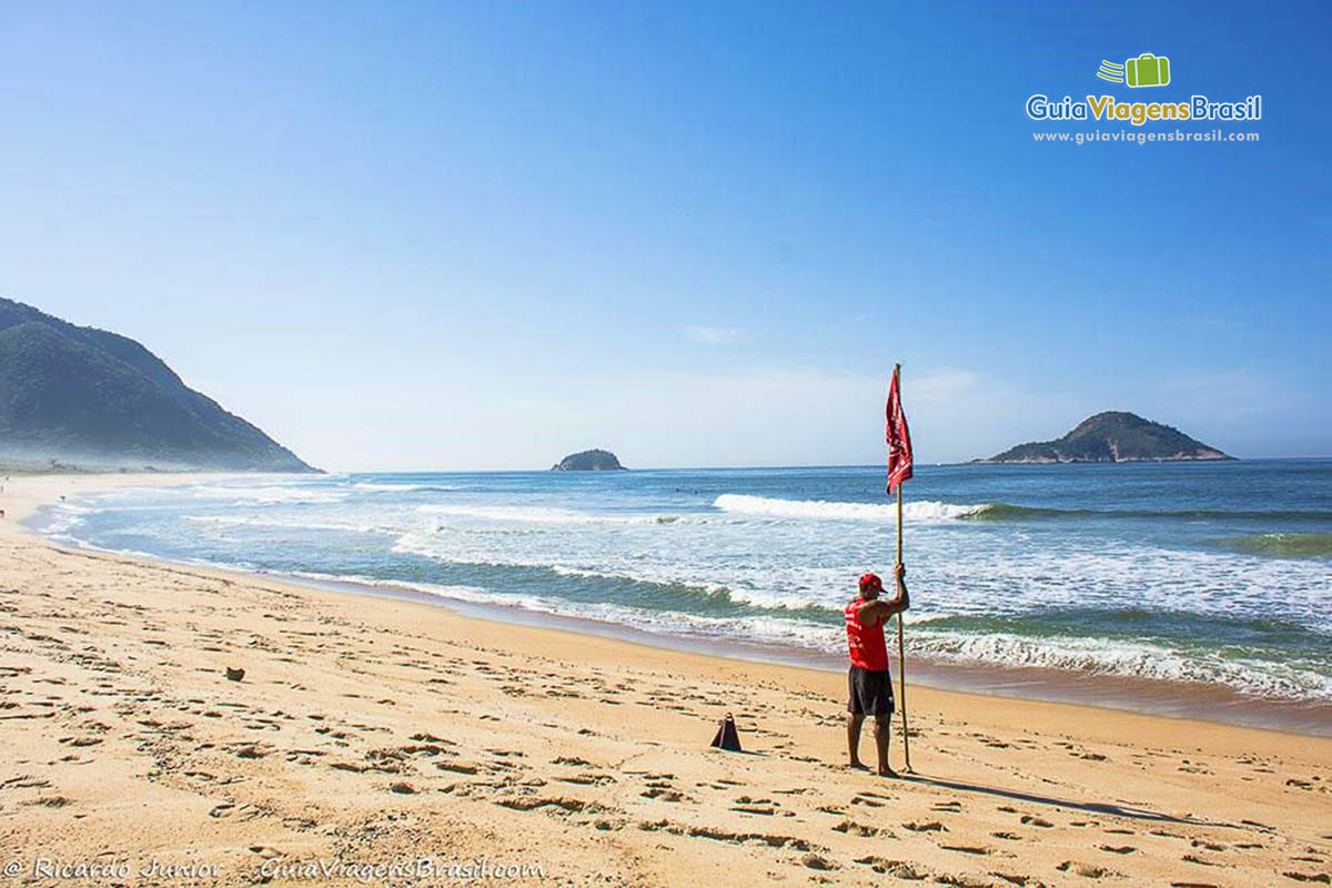 Imagem de salva vidas colocando bandeira vermelha de alerta para os visitantes.