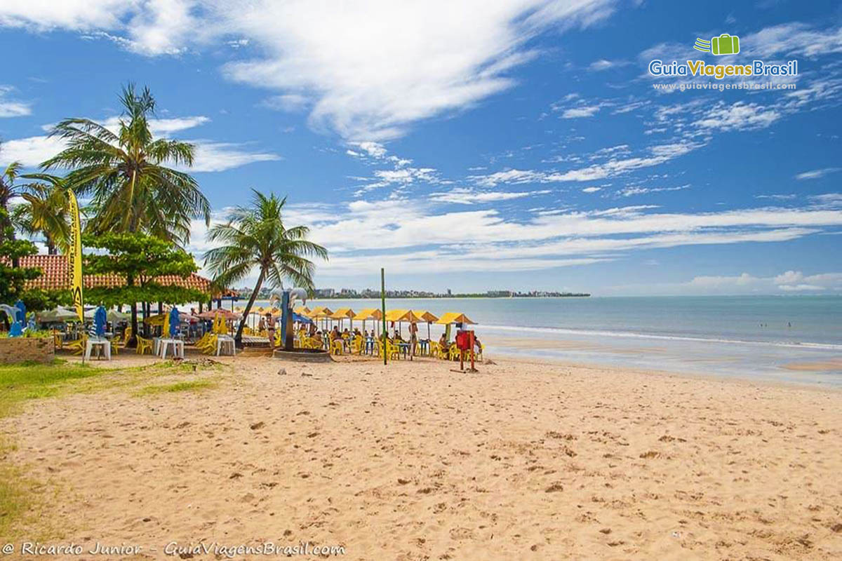 Imagem de bar na beira da praia com cadeiras e guarda sol para os visitantes.