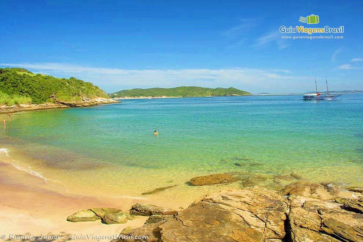 Imagem da praia e ao fundo no mar um barco.