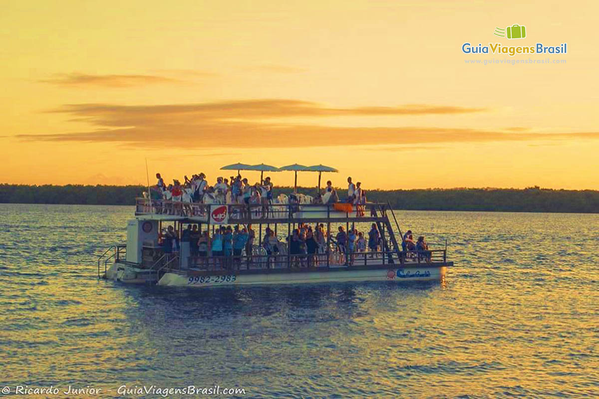 Imagem de barco de passeio com turistas nas águas da Praia Jacaré.