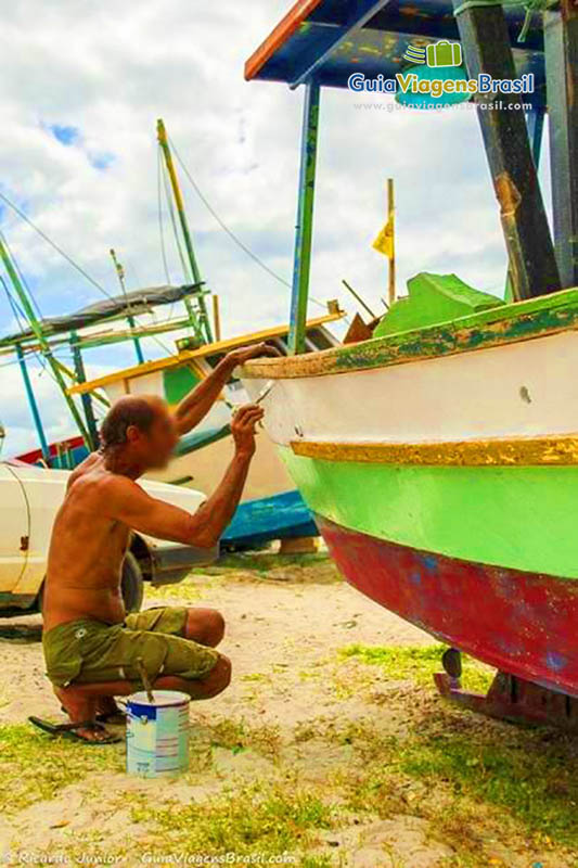 Imagem de um pescador pintando o seu barco.