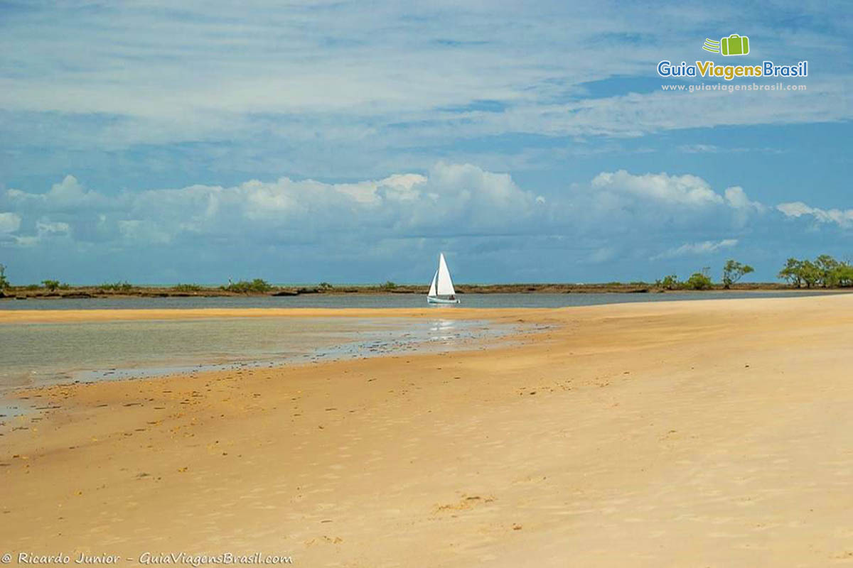 Imagem das areias da praia e ao fundo barco a vela.