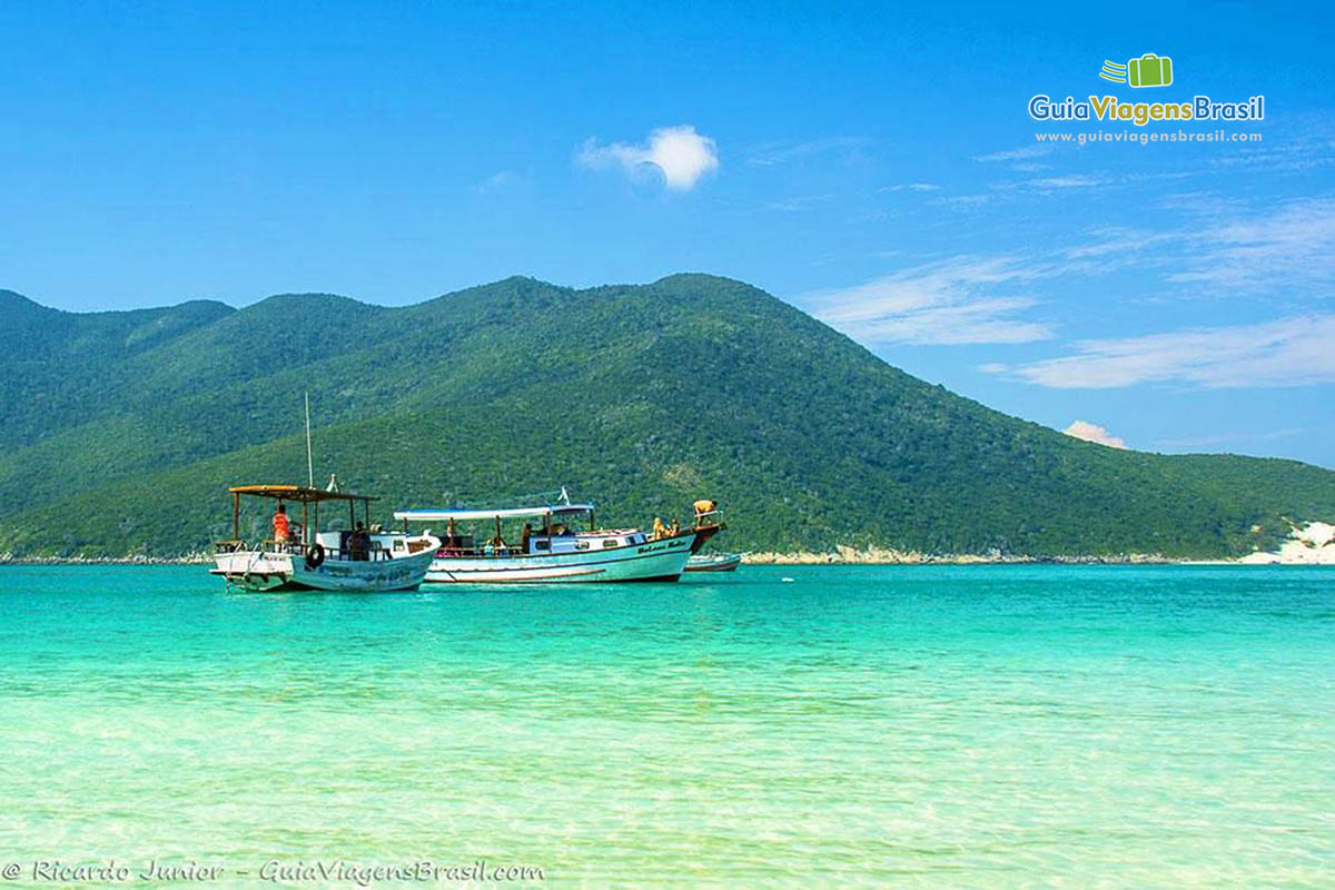 Imagem de barcos e ao fundo morro lindo na Praia Pontal do Atalaia.