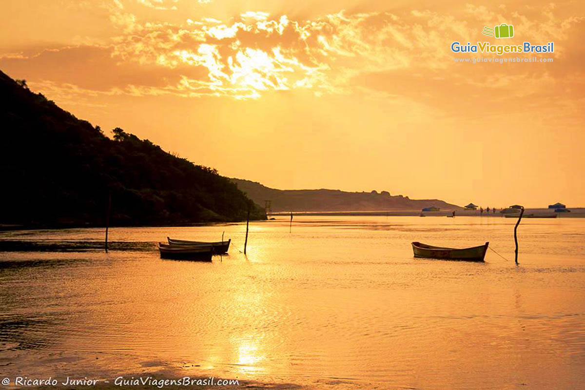 Imagem de três barcos no mar com sol alaranjado refletindo nas águas do mar.