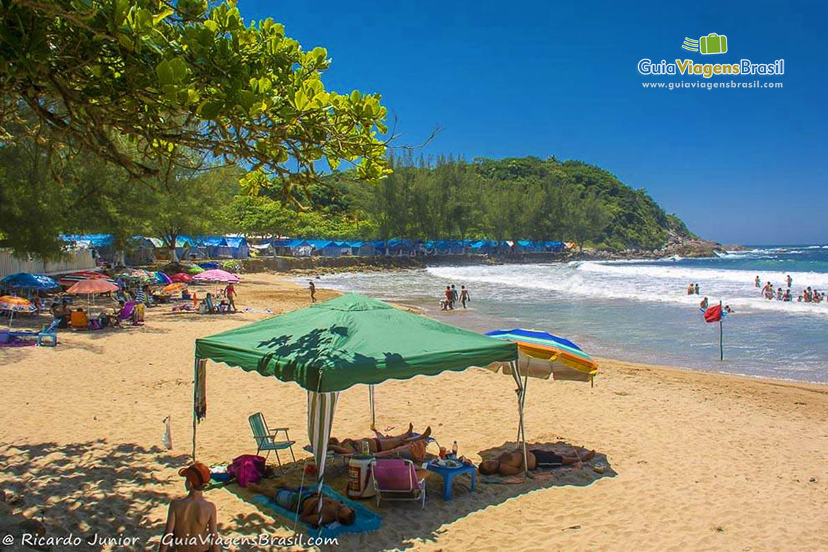 Imagem de uma barraca com pessoas deitadas em baixo para descansar na praia.