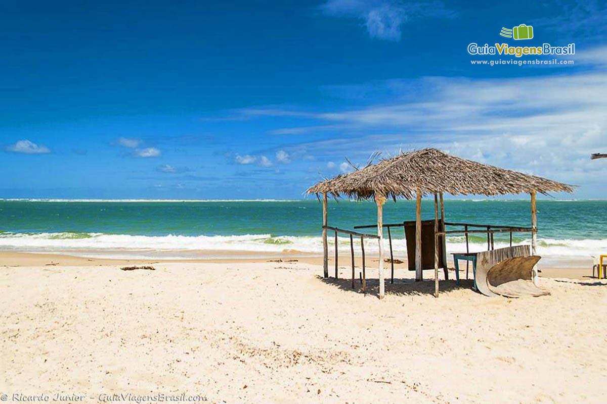 Imagem de uma barraca no meio da areia branca e ao fundo belo mar.