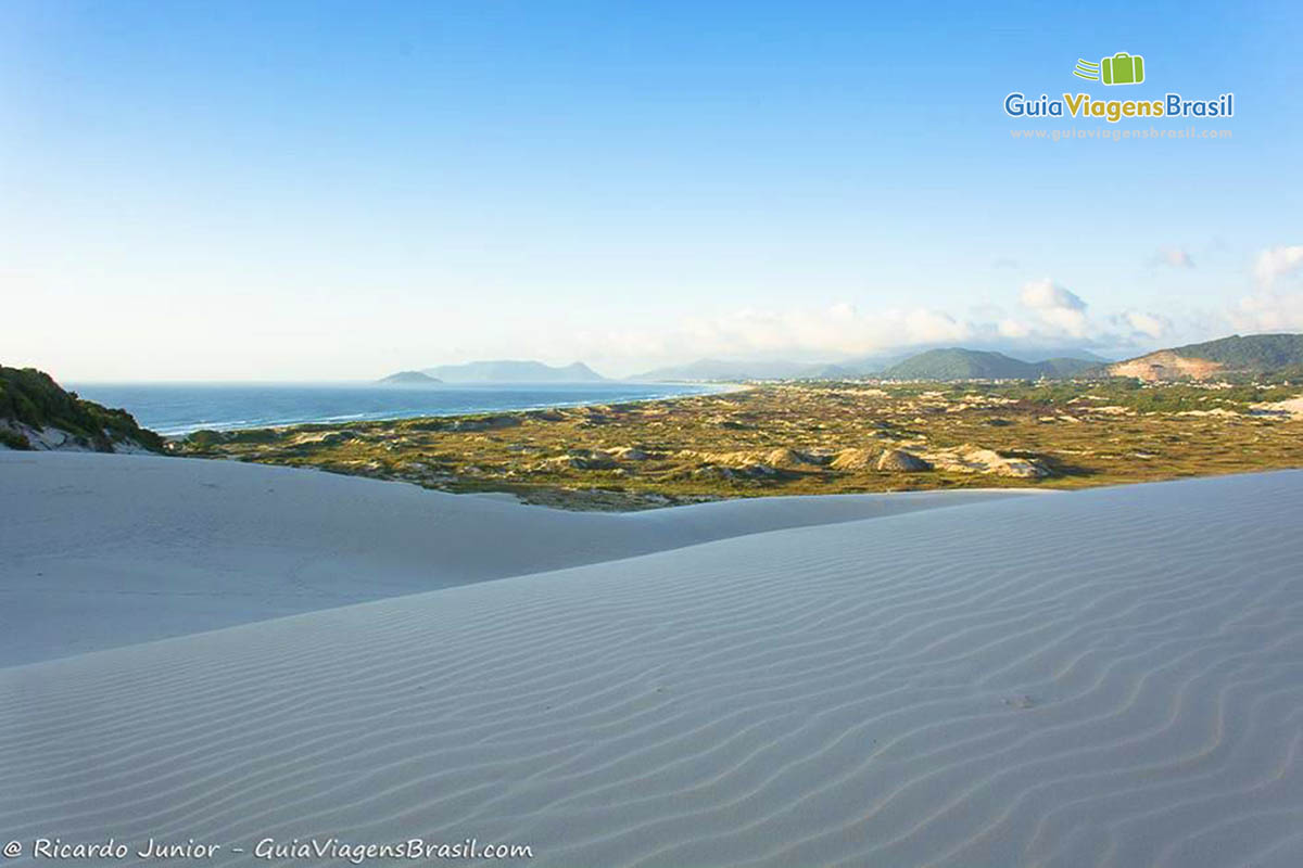 Imagem de dois morros de areia branquinha e ao fundo verde das árvores. 