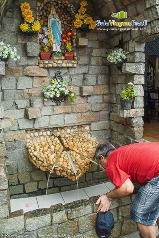 Imagem de fiéis bebendo água da bica que fica no santuário.