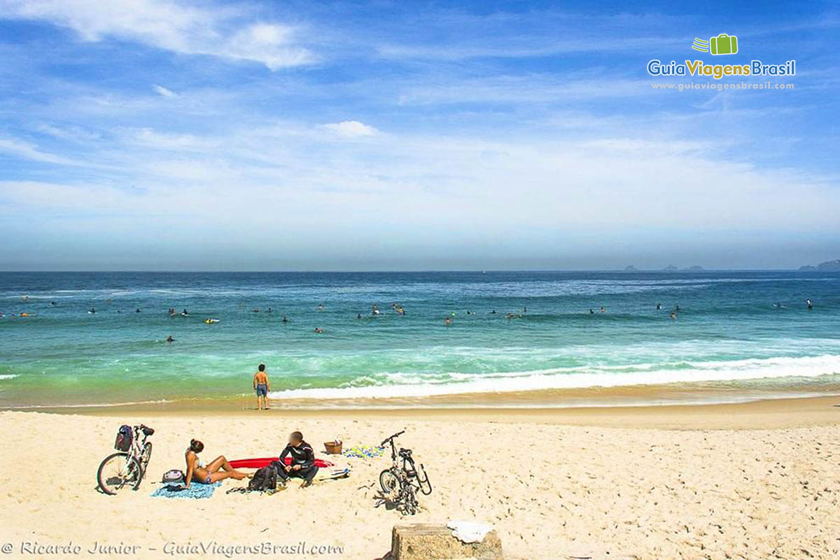 Imagem de um casal sentados na areia e ao lados suas bicicletas.