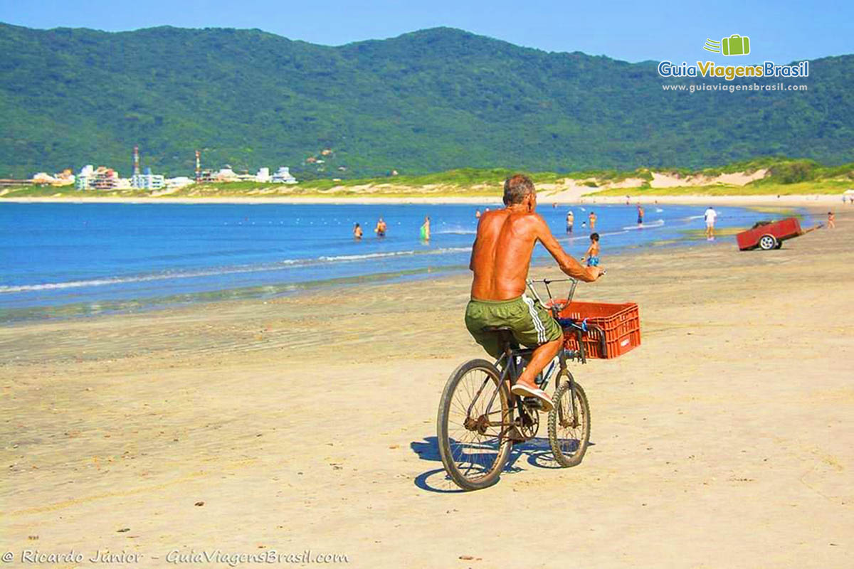 Imagem de uma pessoas andando de bicicleta na areia da praia.