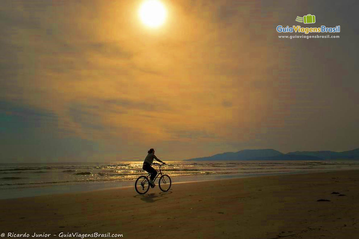 Imagem de uma pessoa andando de bicicleta no fim de tarde na praia.
