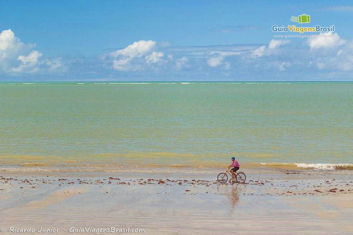 Imagem de uma pessoa andando de bicicleta na beira da praia.