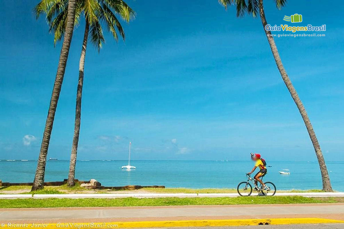 Imagem de um rapaz andando de bicicleta pela orla da Praia Ponta Verde.