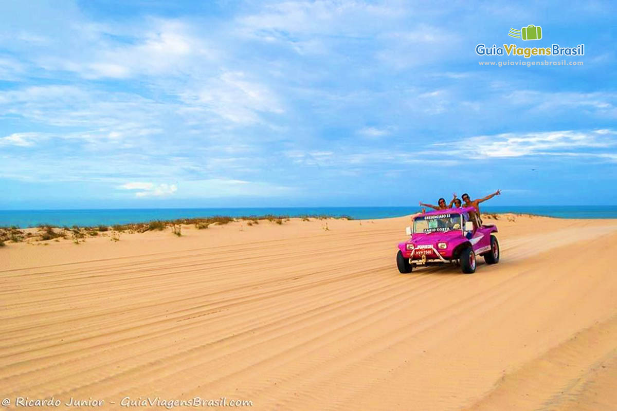 Imagem de bugue rosa andando pelas Dunas e ao fundo o mar azul de Canoa Quebrada.