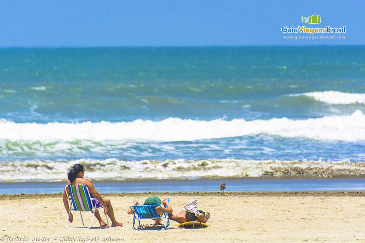 Imagem de turistas sentados na cadeira nas areias da Praia de Itanhaem.