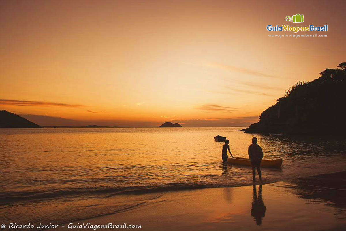 Imagem de duas pesssoas próximas a um caiaque na bela imagem de fim de tarde na praia.