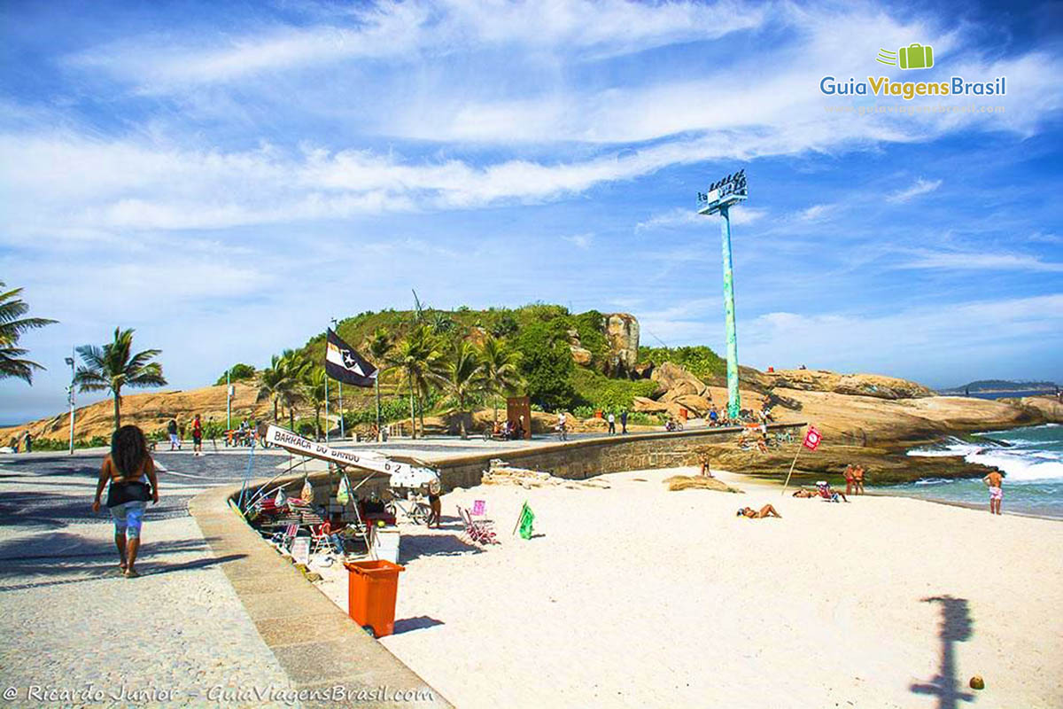 Imagem de pessoas no calçadão da praia e nas areias do Arpoador.