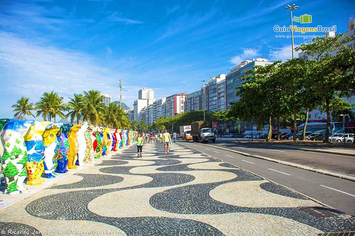 Imagem de esculturas coloridas no calçadão e pessoas fazendo caminhadas.