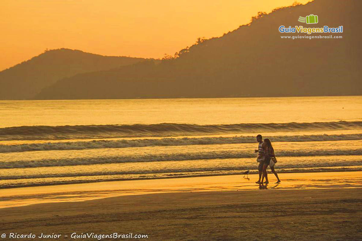 Imagem de pessoas caminhando na beira da praia e um fim de tarde maravilhoso.