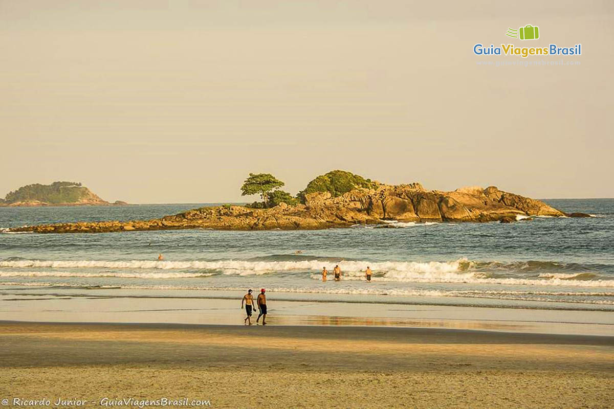 Imagem de dois homens caminhando na beira do mar na Praia Astúrias.