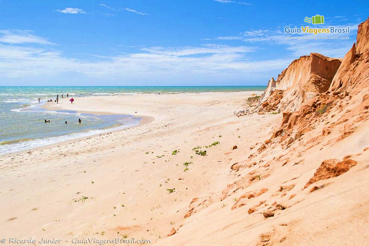 Imagem de turistas aproveitando o belo mar azul da praia.