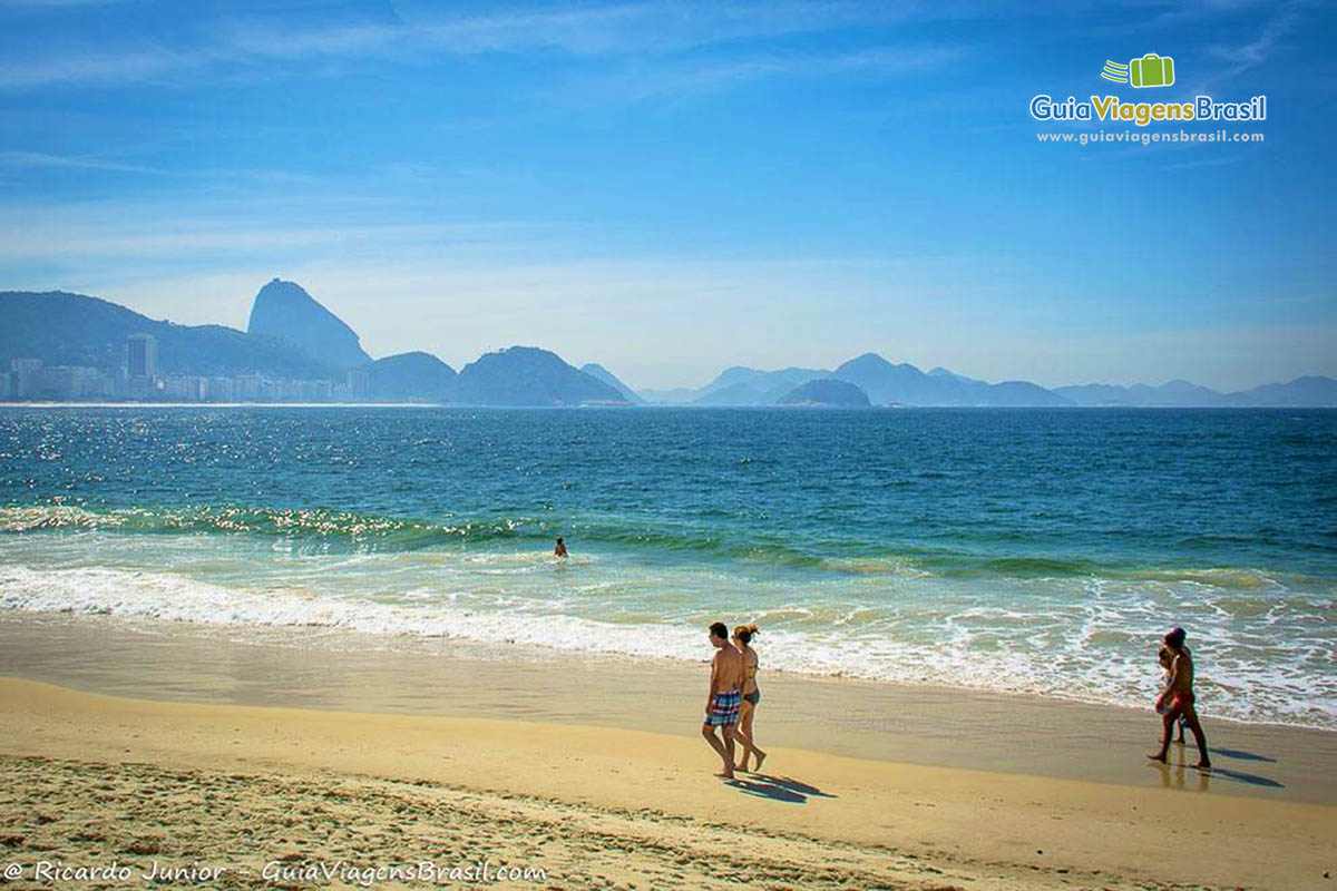 Imagem de casal e amigos andando nas areias da Praia de Copacabana.