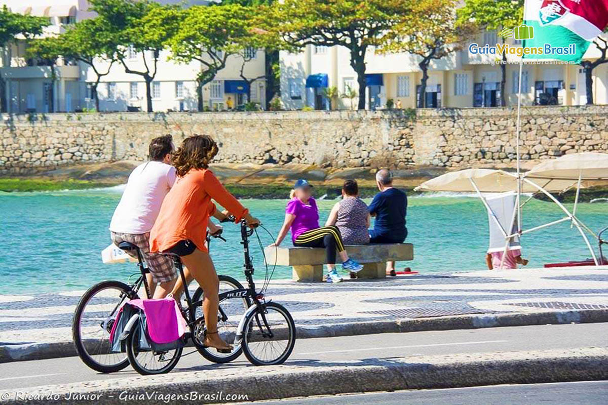 Imagem de casal andando de bicicleta na orla da praia.