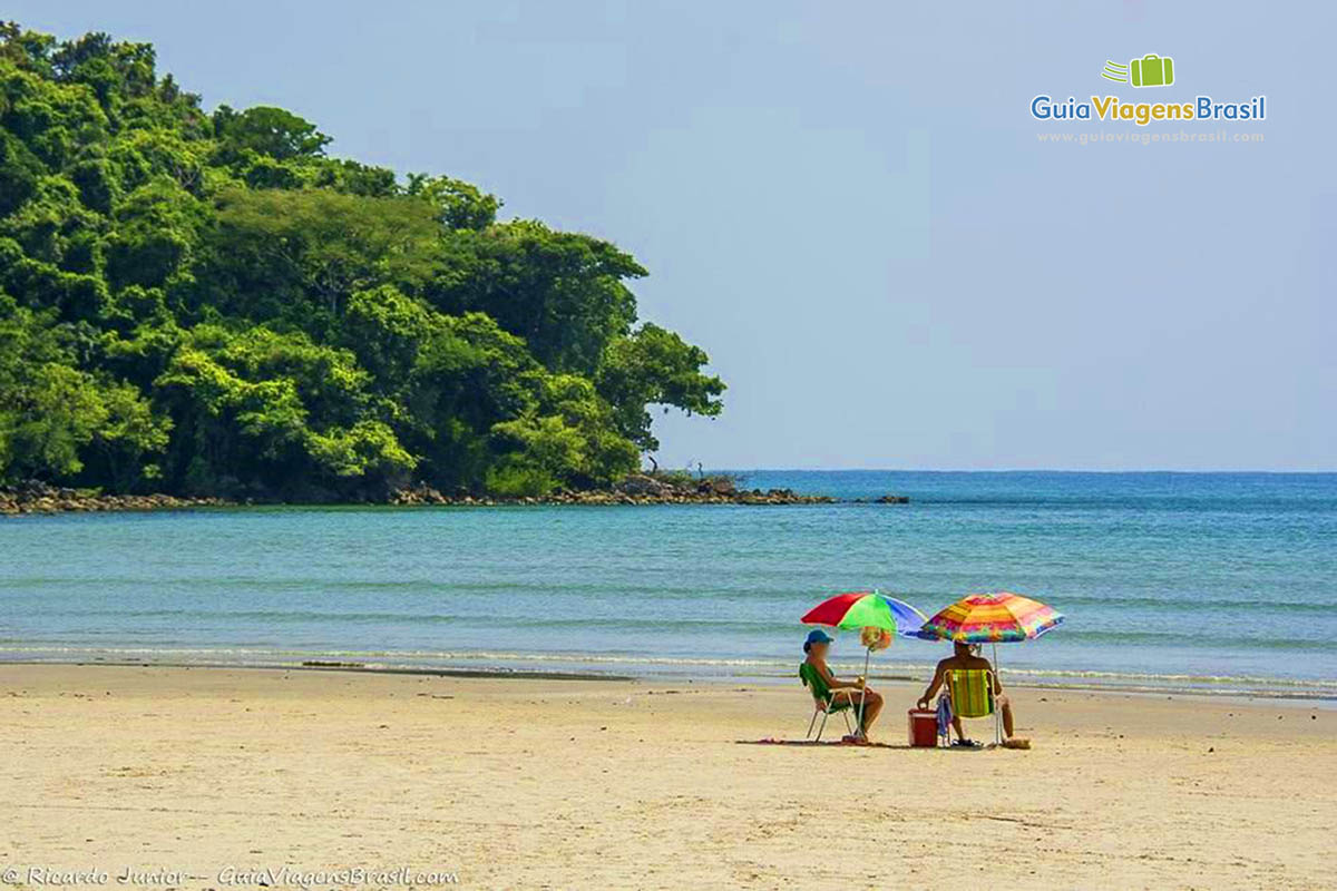 Imagem de casal sentados curtindo a linda praia.