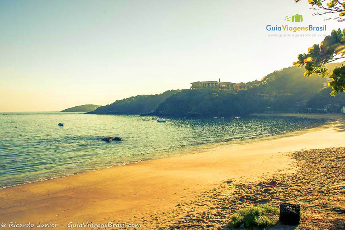 Imagem de uma tarde de sol na praia e ao fundo belas casa em cima do morro.