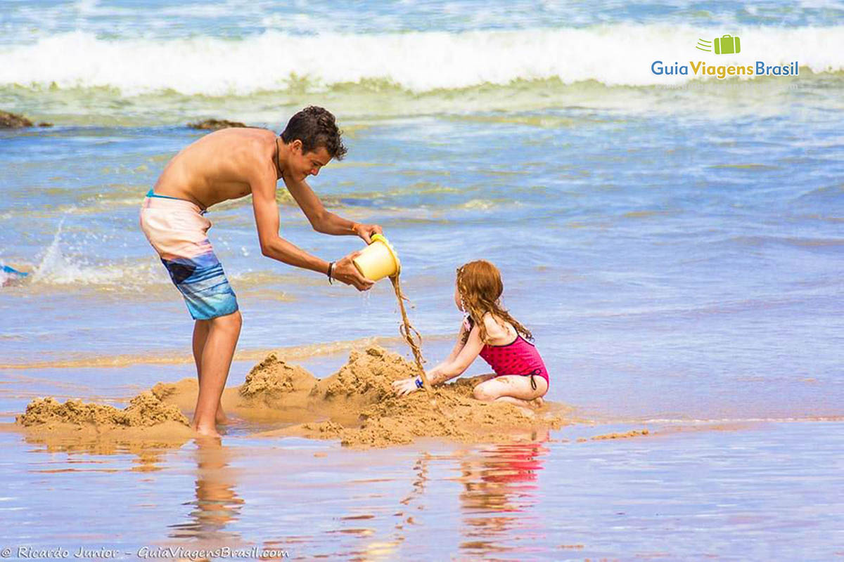 Imagem de menino e menina fazendo castelinho na praia.