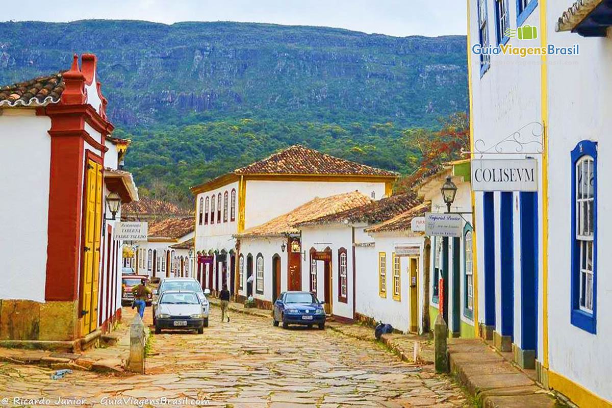 Imagem de carros nas ruas de paralelepípedos e ao fundo belo morro.