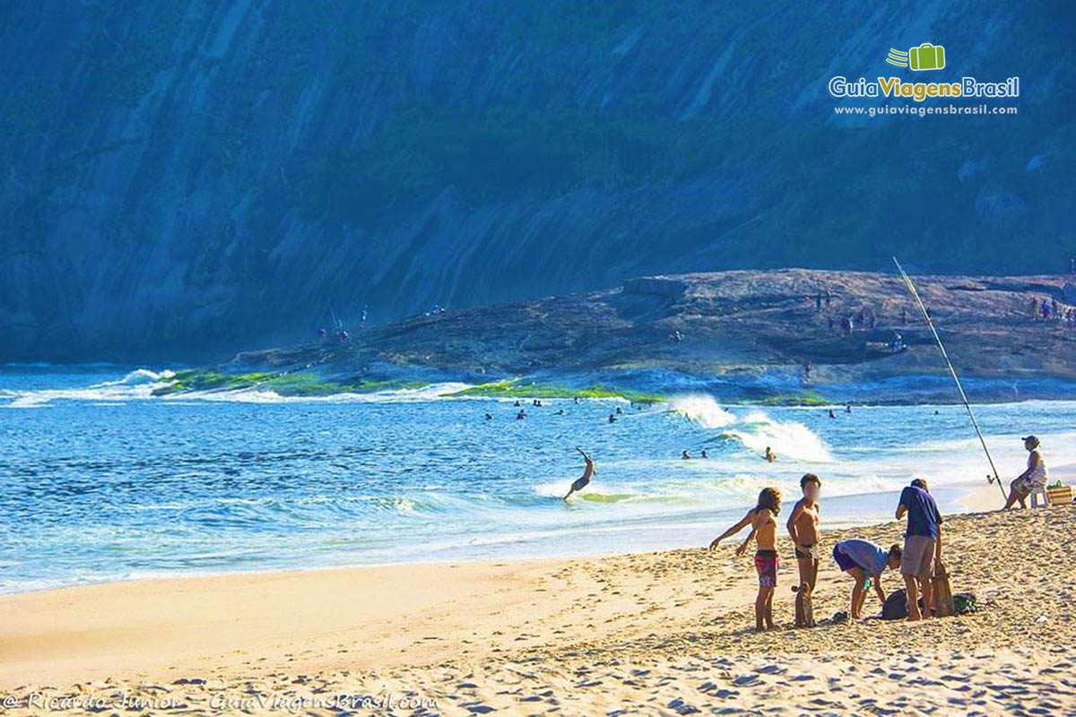 Imagem de pessoas pescando e ao fundo pessoas surfando e nadando nas águas.