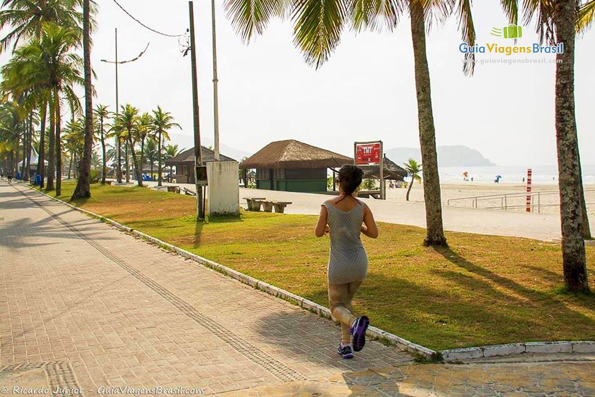 Imagem de uma moça correndo no calçadão da Praia da Enseada.
