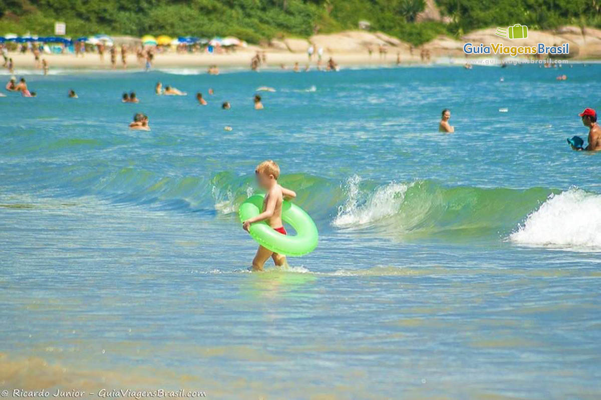 Imagem de uma criança saindo do mar com uma bóia nas cintura.