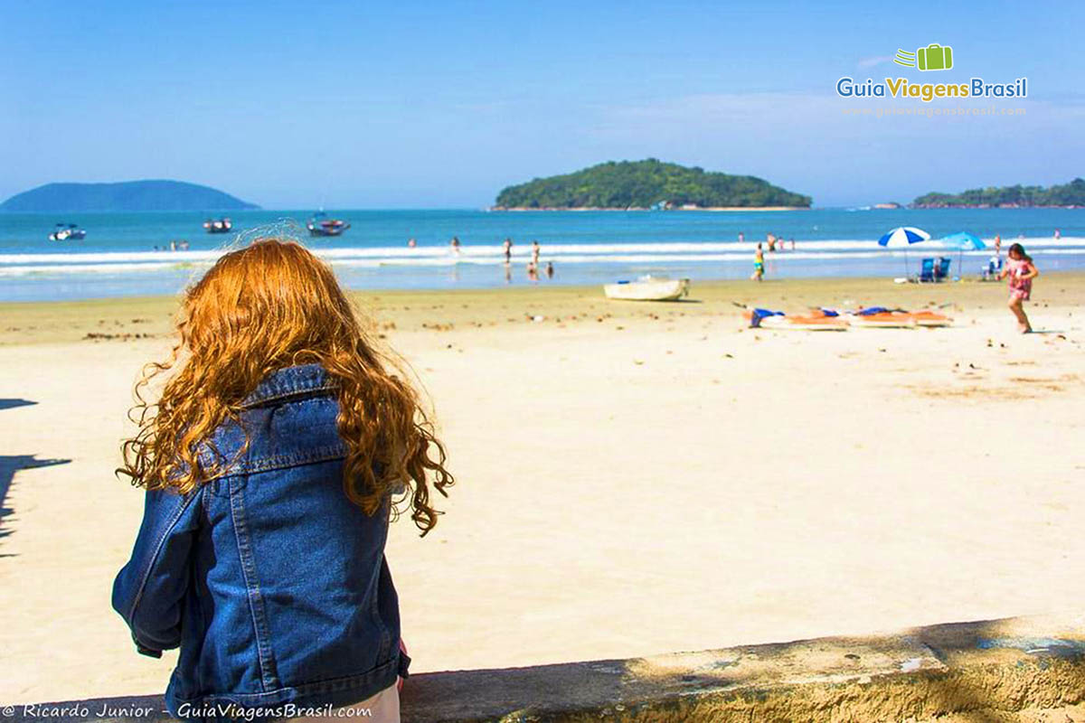 Imagem de uma criança sentada na orla da Praia de Maranduba.