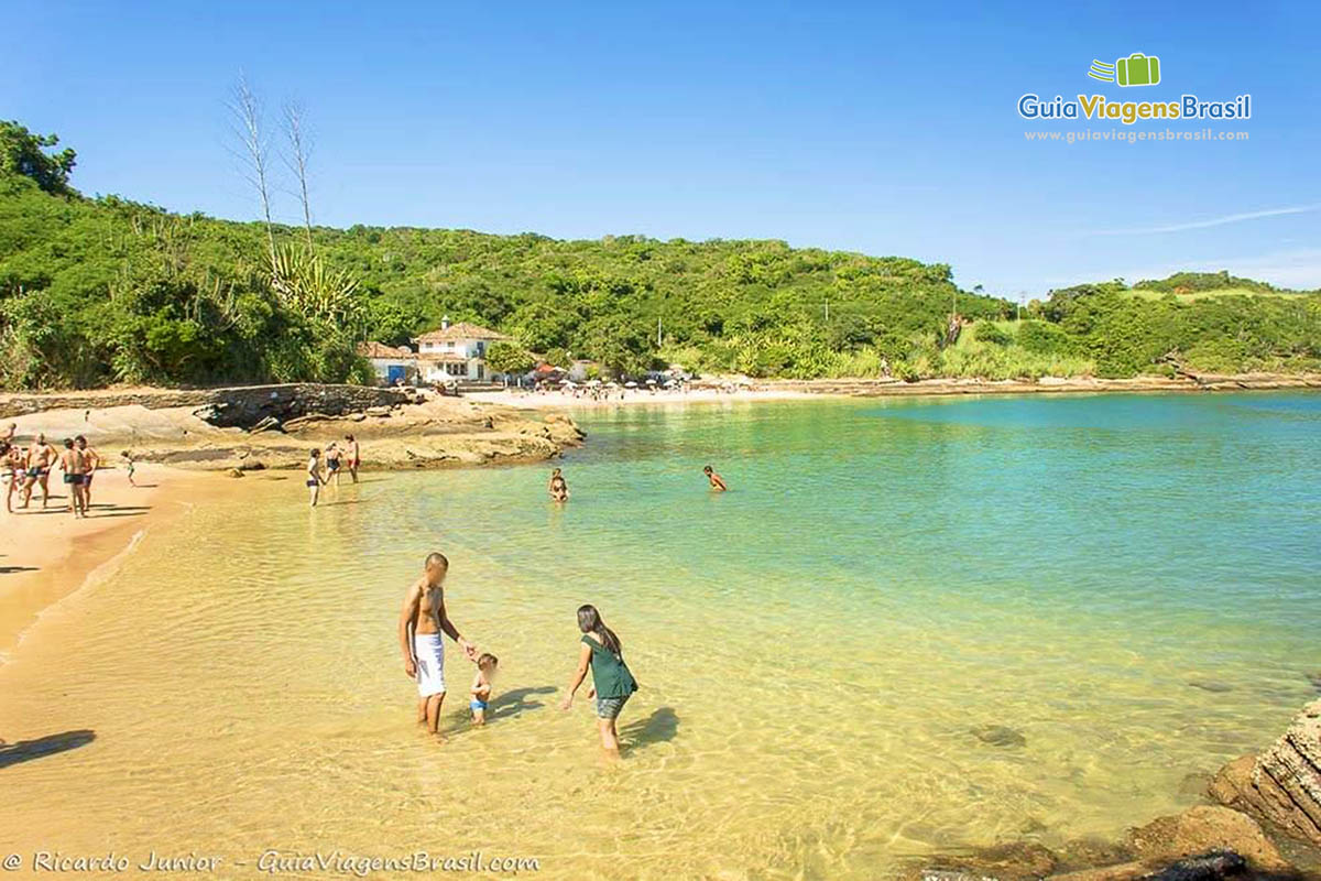 Imagem de criança com os pais na beira da praia se divertindo.