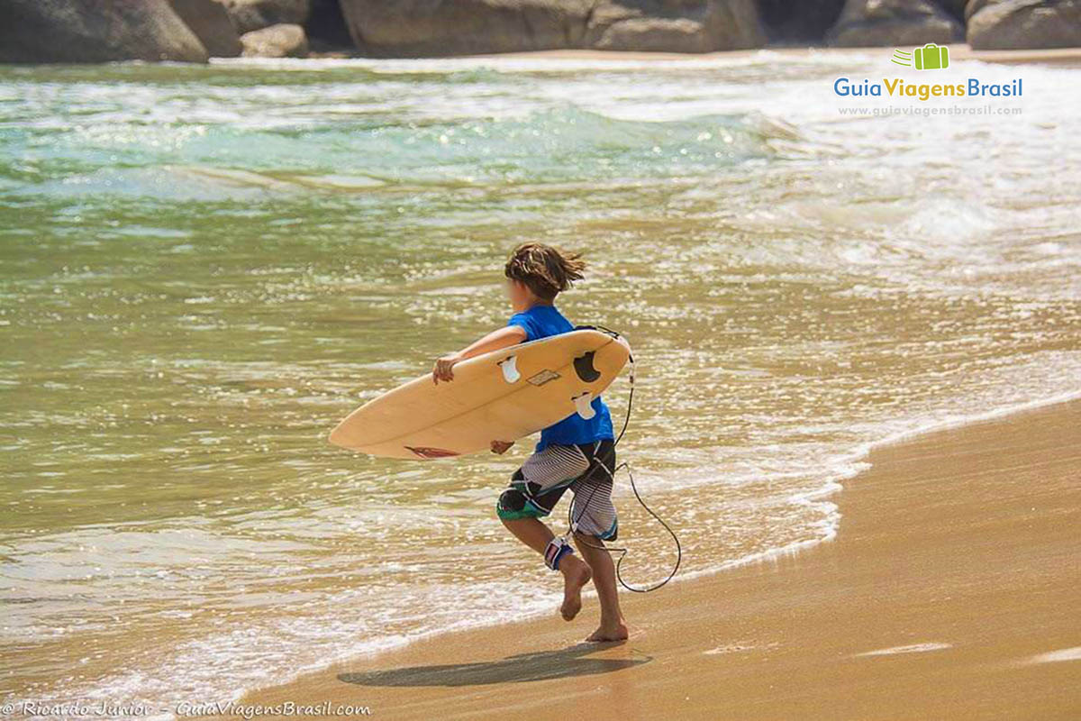 Imagem de um menino correndo com sua prancha para mar na Praia Bonete.