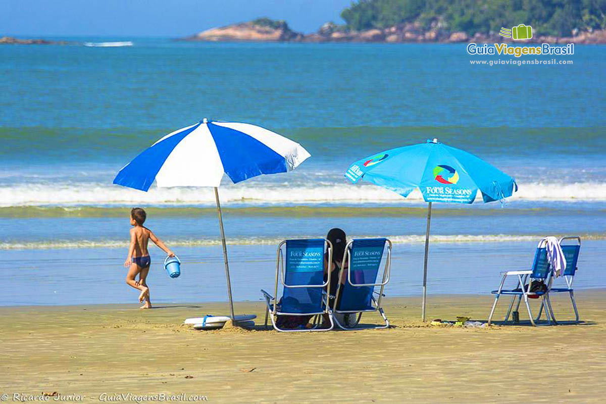 Imagem de criança andando com baldinho  de areia.