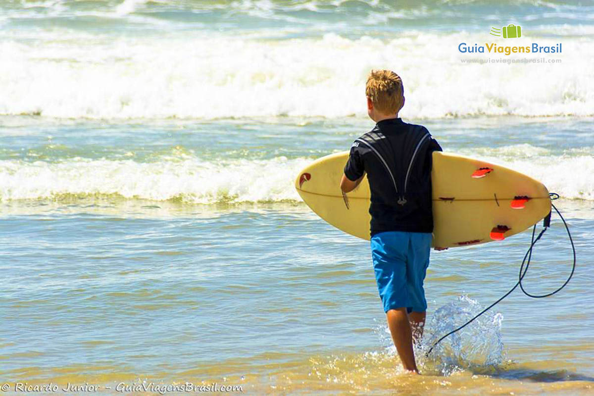 Imagem de um menino entrando na Praia da Ferrugem para pegar onda. 
